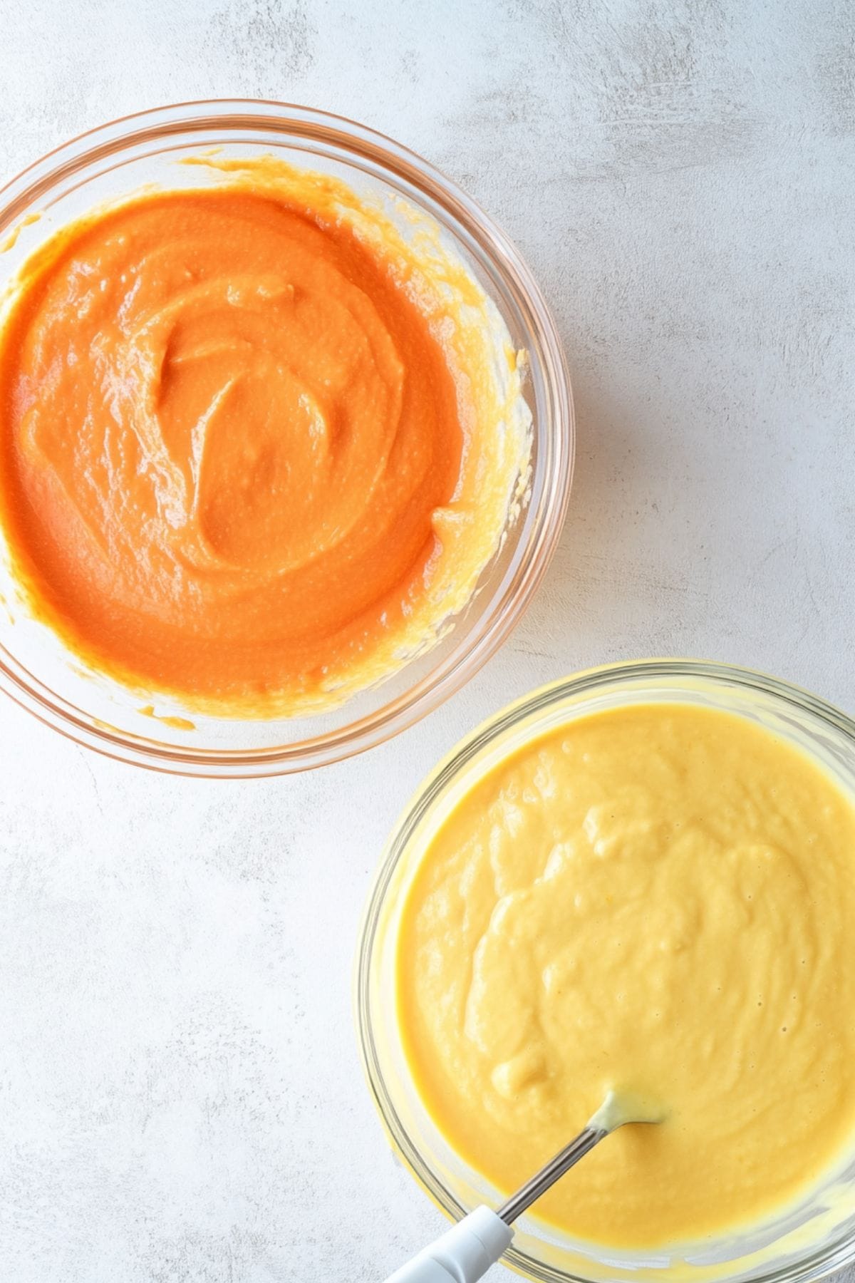 Yellow and orange cake batter in separate glass bowls, top view