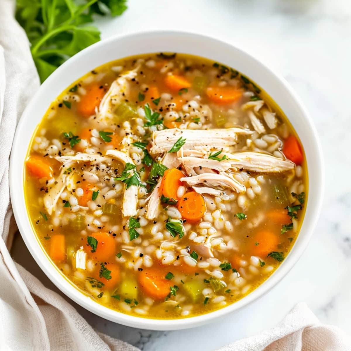 Chicken barley soup in a white ceramic bowl, garnished with fresh parsley.