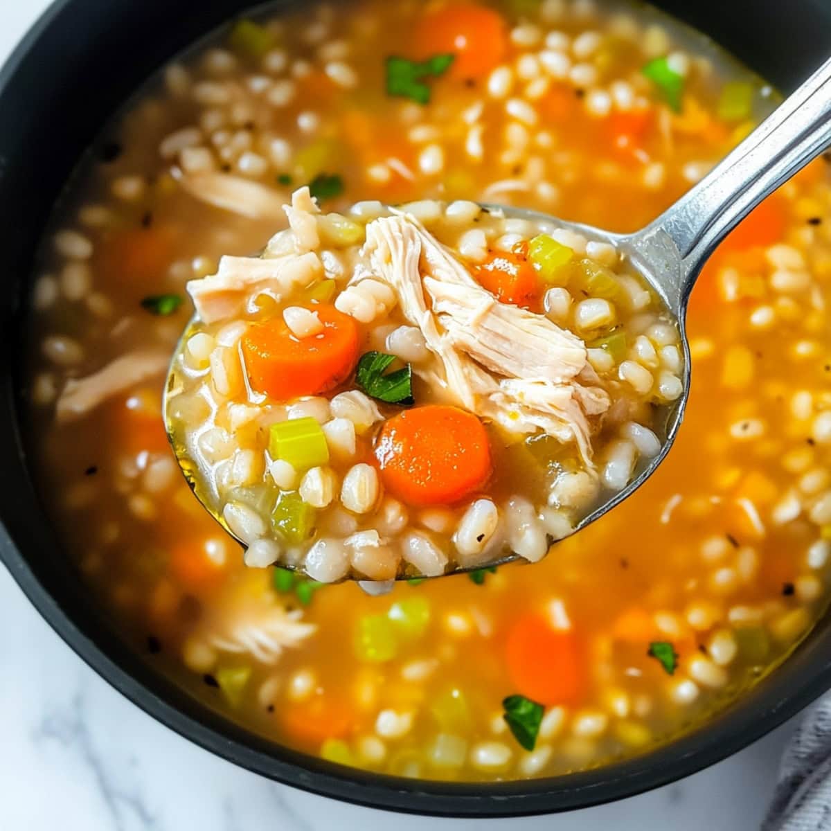 A spoonful of chicken barley soup with carrots and celery.