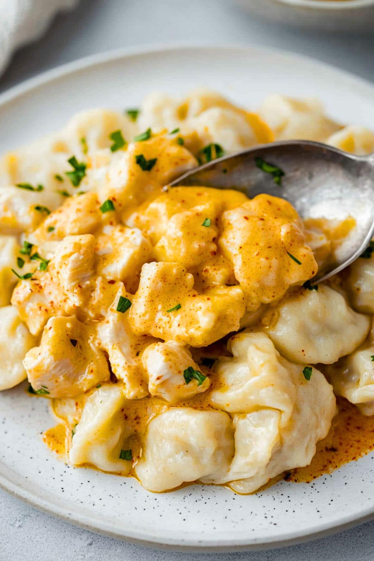 Spoon scooping some serving of chicken with paprika infused sauce served on top of flour dumplings served in white plate.