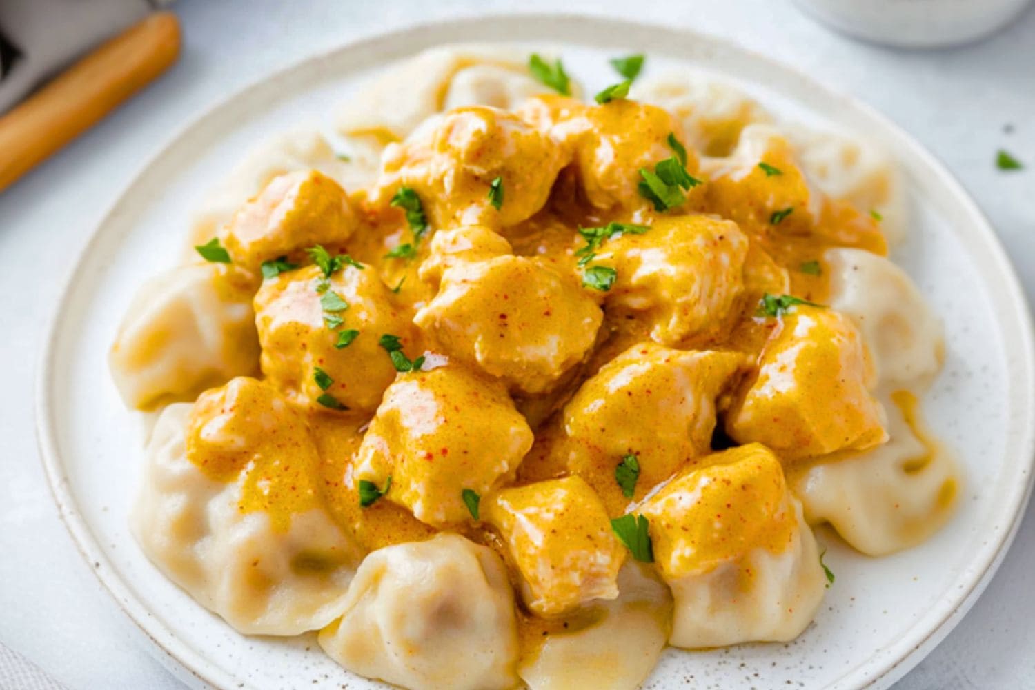 Flour dumplings topped with chicken paprikash served on a white plate.