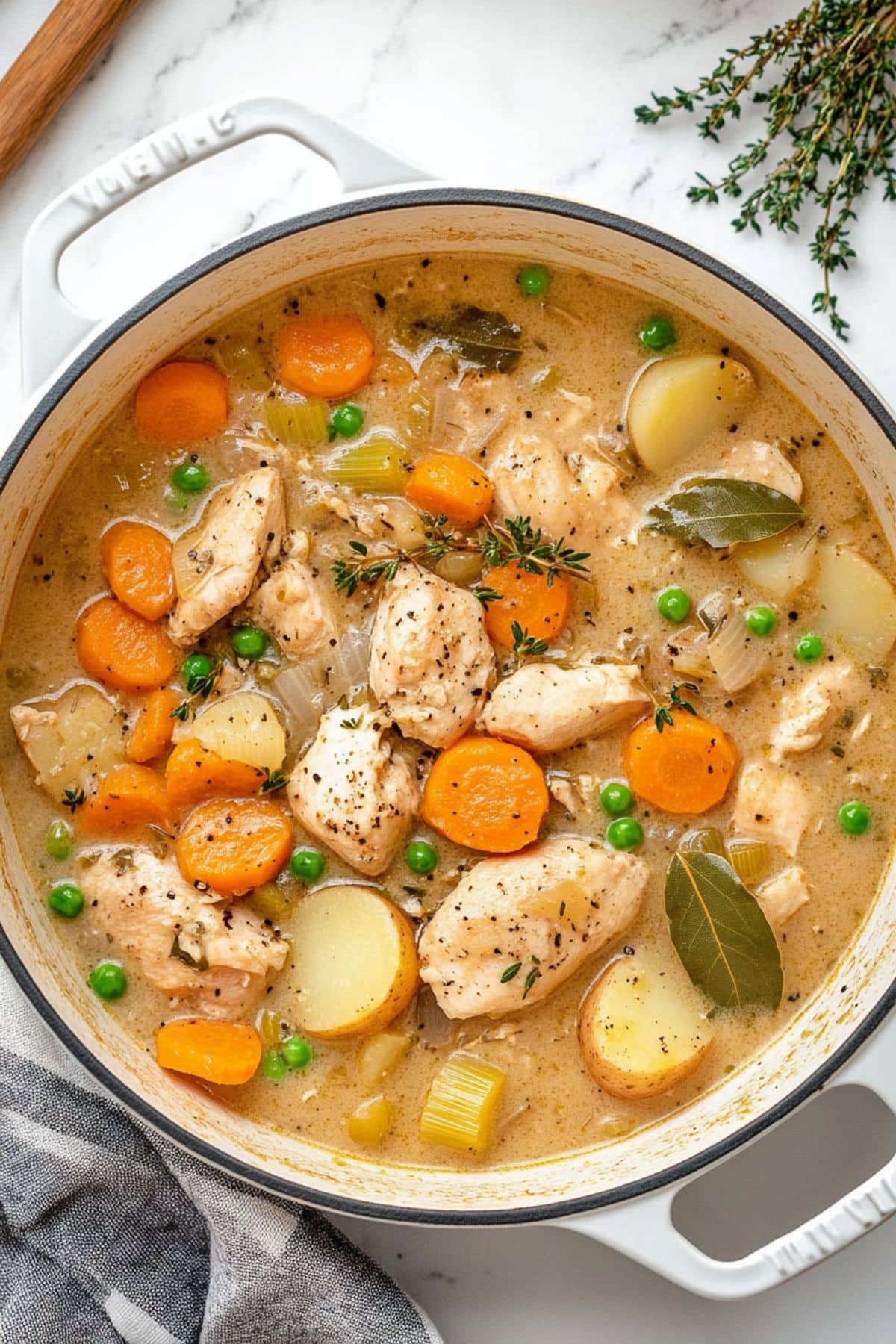 Chicken stew in a white Dutch pot with sliced carrots, marble potatoes and herbs.