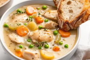 A serving of chicken stew in creamy thick sauce, sliced potatoes, carrots and green peas.