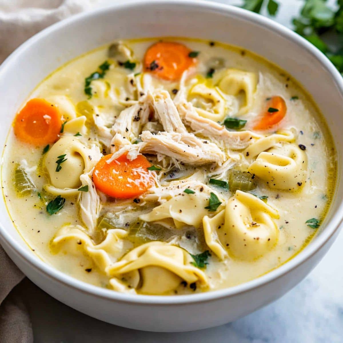 Chicken tortellini soup with shredded chicken, pasta, carrots in creamy soup served in a white bowl.