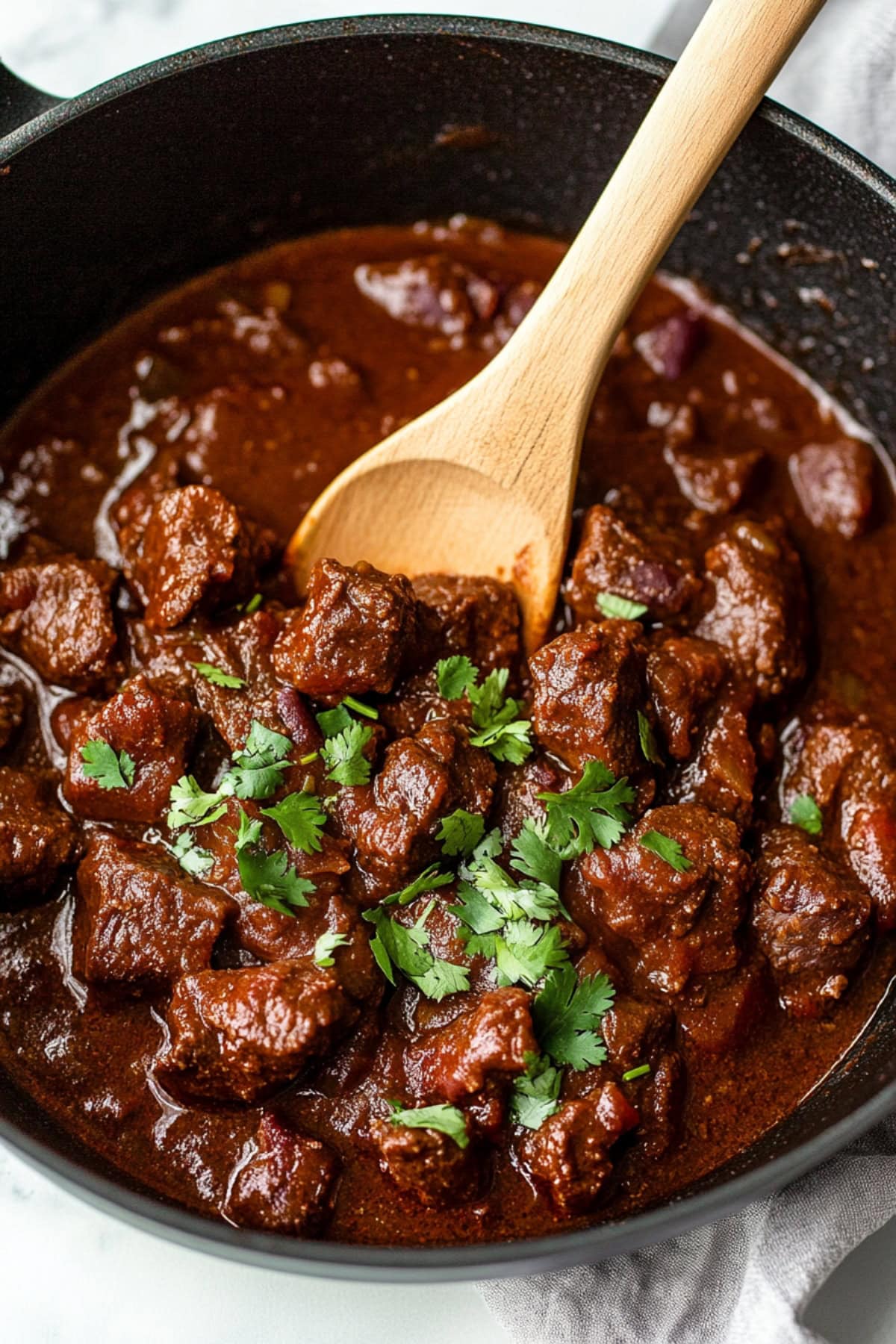 Chili Colorado with tender beef chunks, and garnished with chopped cilantro in a black skillet.