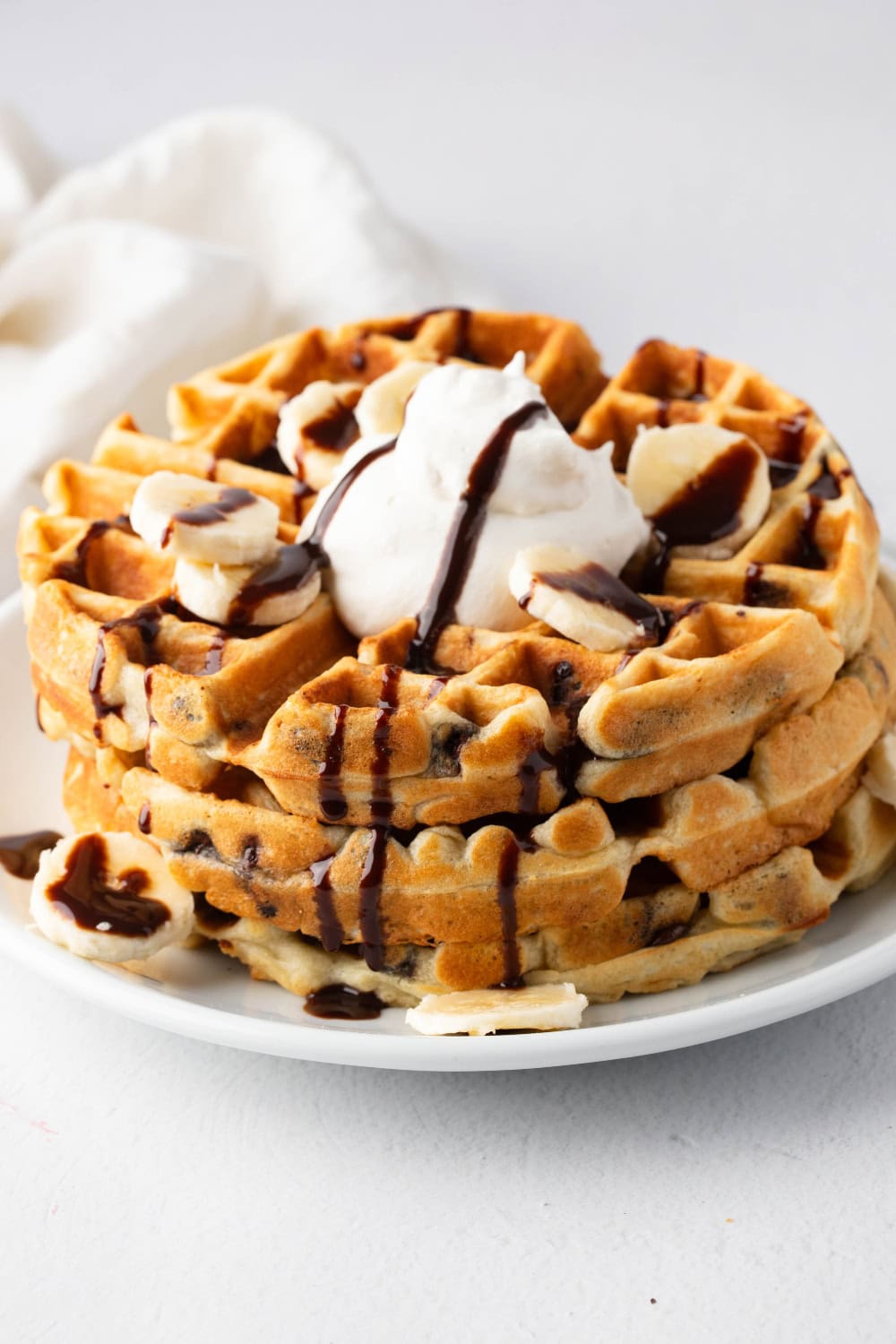 Stack of chocolate chip waffles topped with chocolate sauce, whipped cream, and banana slices