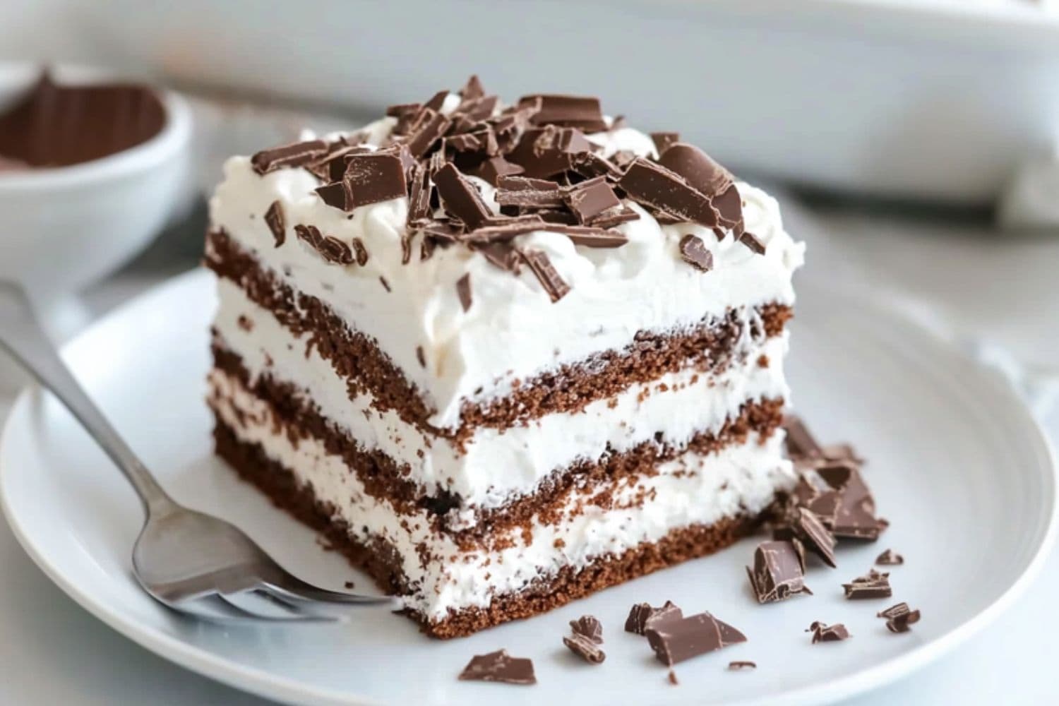 Square slice of chocolate icebox cake served in a white plate garnished with chocolate shavings.