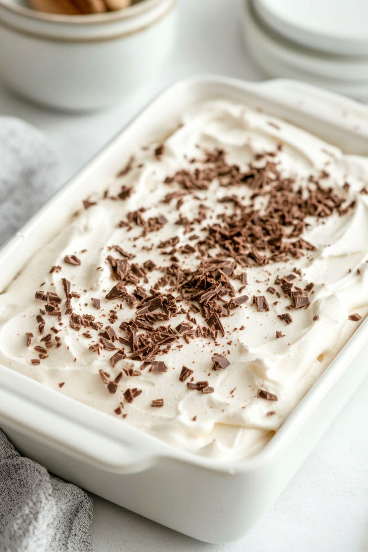 Whipped cream covered cake garnished with chocolate shavings in a baking dish.