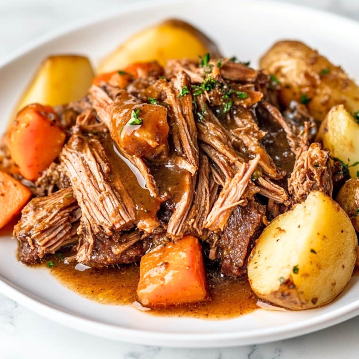 Shredded pot roast served in a white plate with potatoes and carrots.