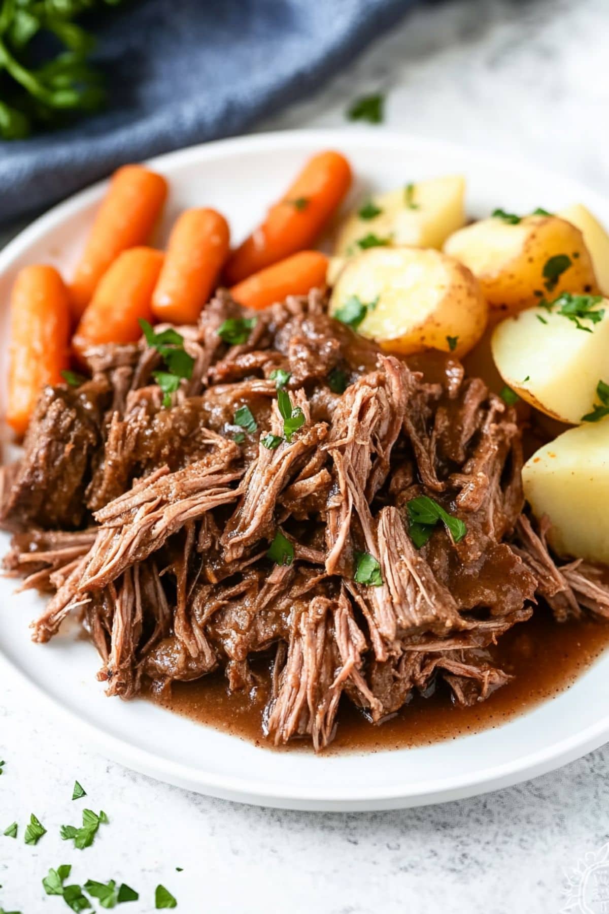 Shredded roast chuck in a white plate served with potatoes and carrots.