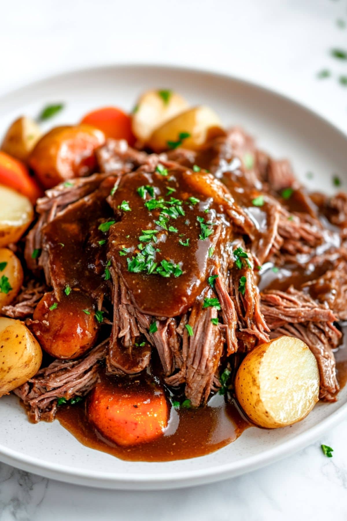 Shredded chuck roast with carrots and potatoes served on a white plate