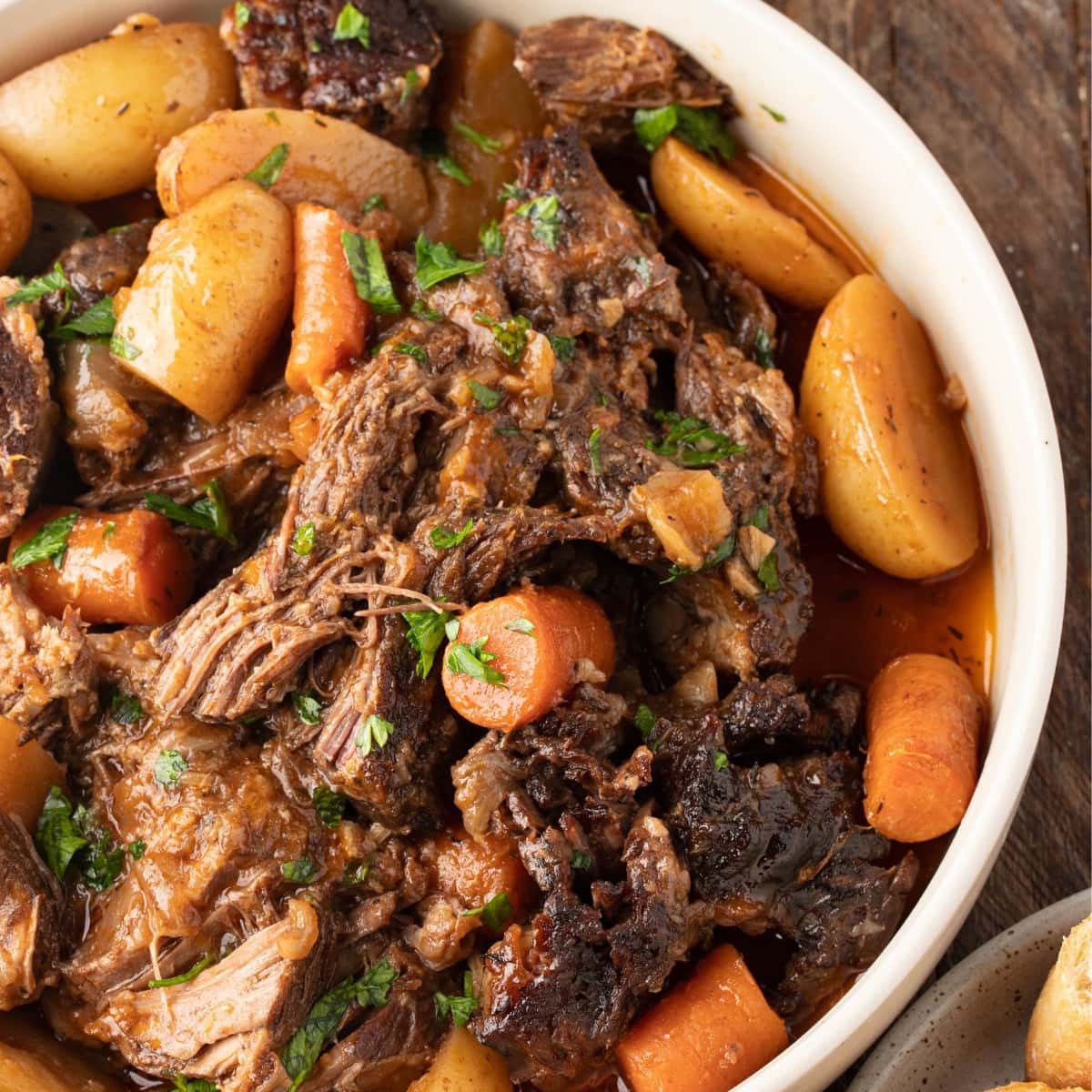 Pot roast with sliced carrots and potatoes in a white bowl.