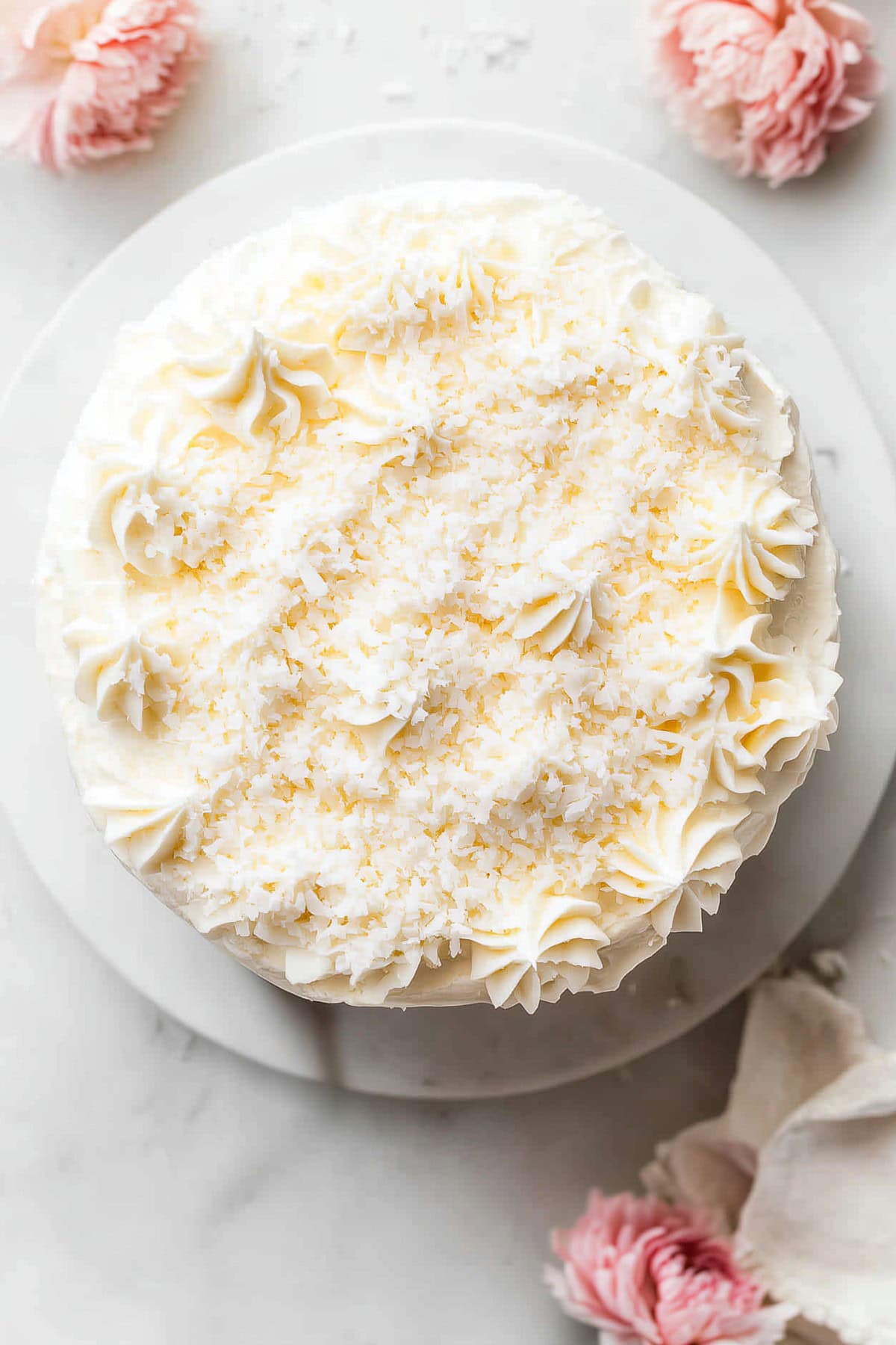 A whole coconut cake with cream cheese frosting on a plate, top view