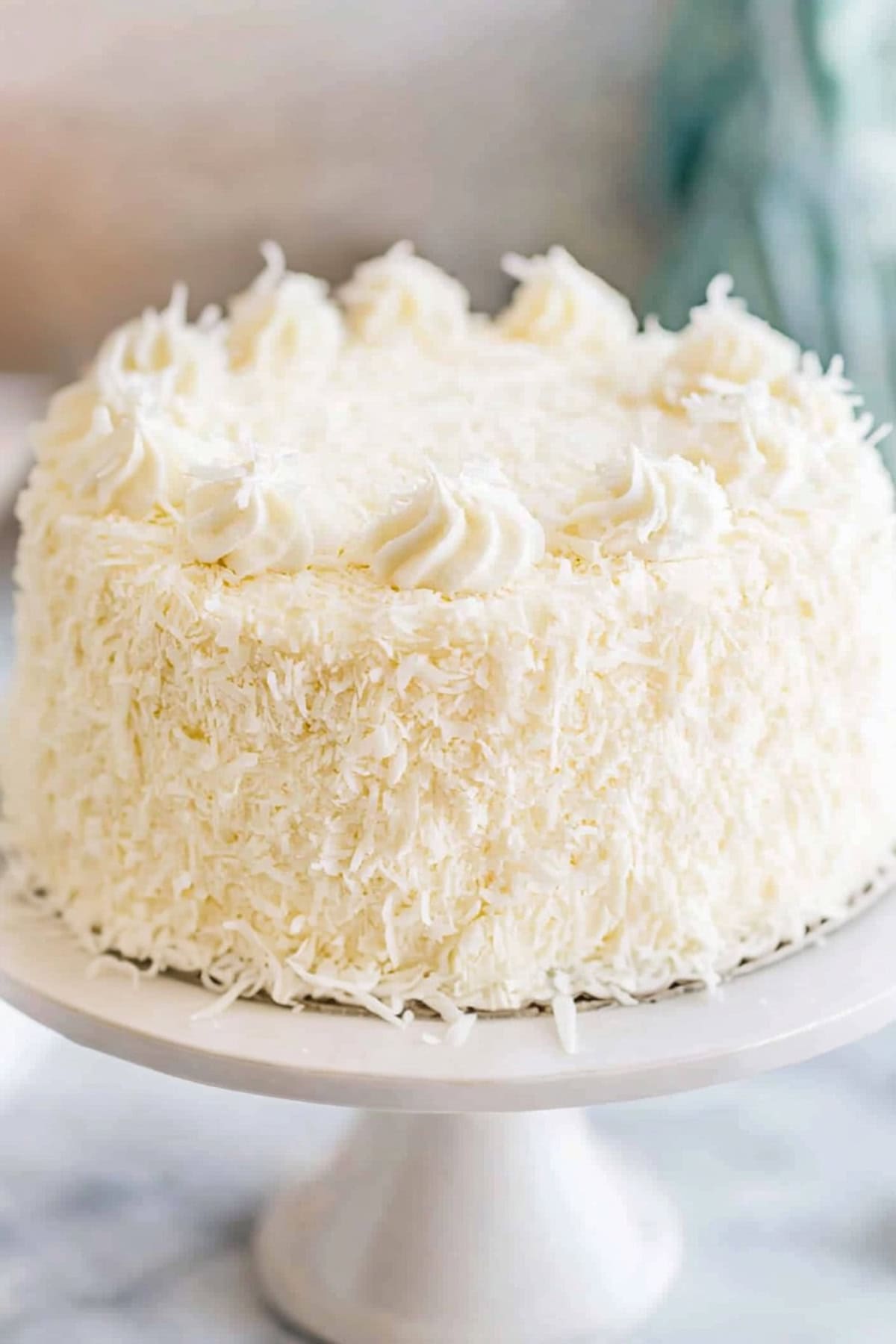 Whole coconut cake with cream cheese frosting in a cake stand.