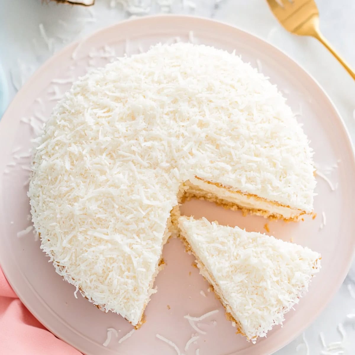 Creamy and dreamy coconut cake being  sliced in a plate.