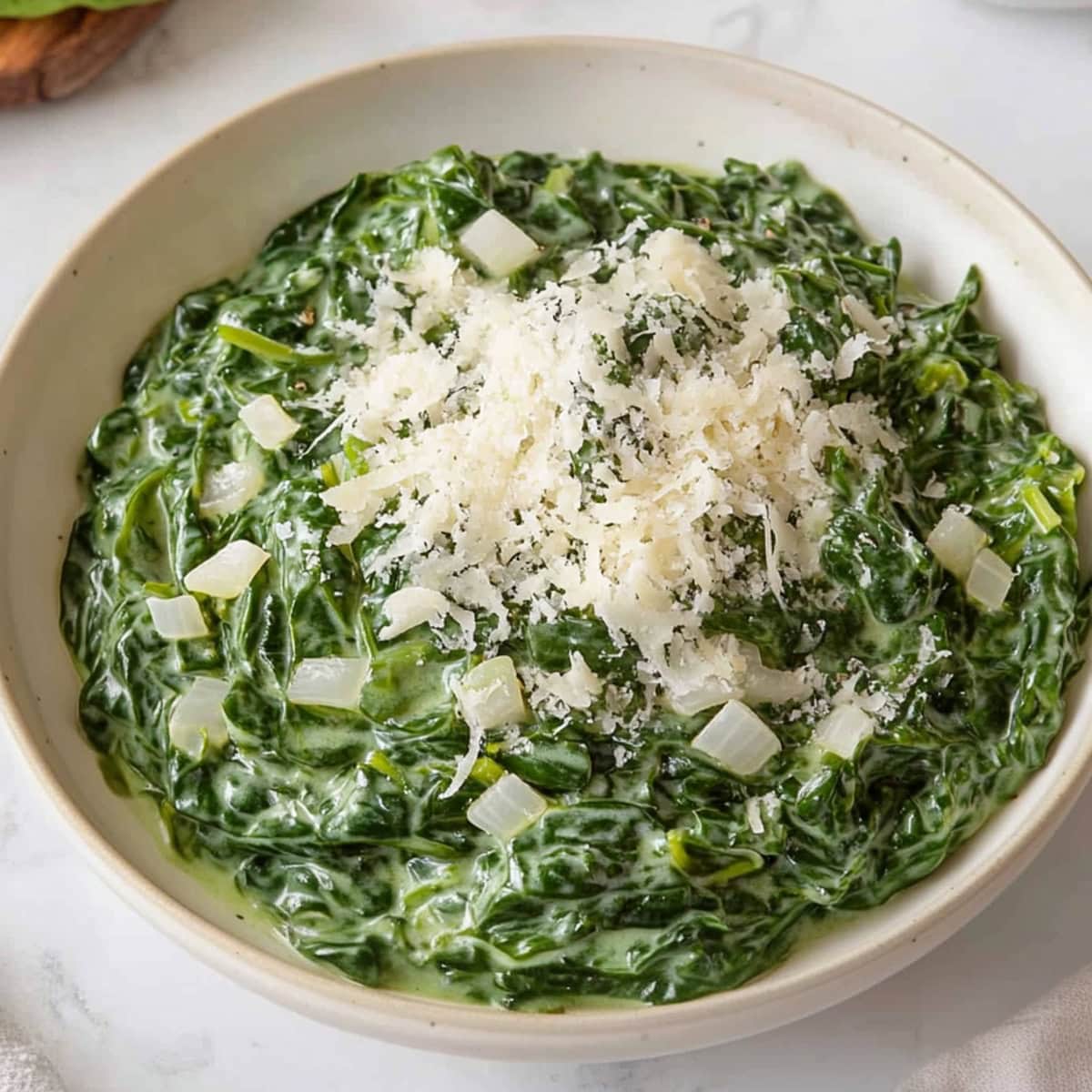 Silky creamed spinach in a white bowl, topped with a sprinkle of Parmesan cheese.