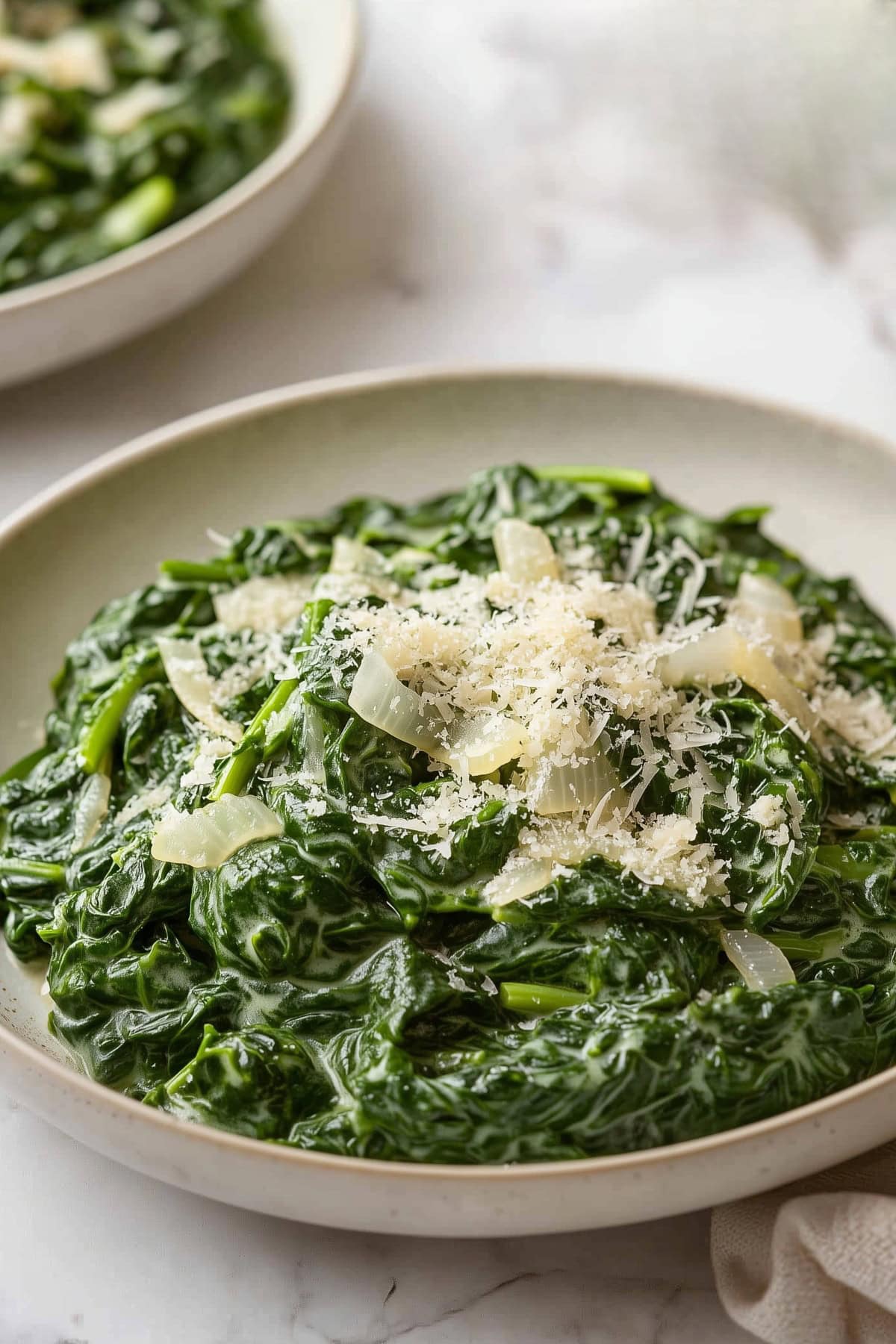 A close-up of creamy spinach with flecks of garlic and onion, served in a bowl.