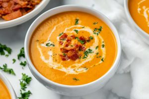 Warm, thick carrot soup served with a sprig of parsley, crispy bacon and cracked pepper on top.