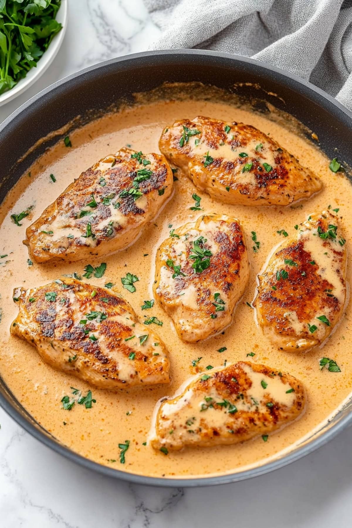 Close-up of golden-brown chicken lazone smothered in a rich, creamy sauce on a white dish.