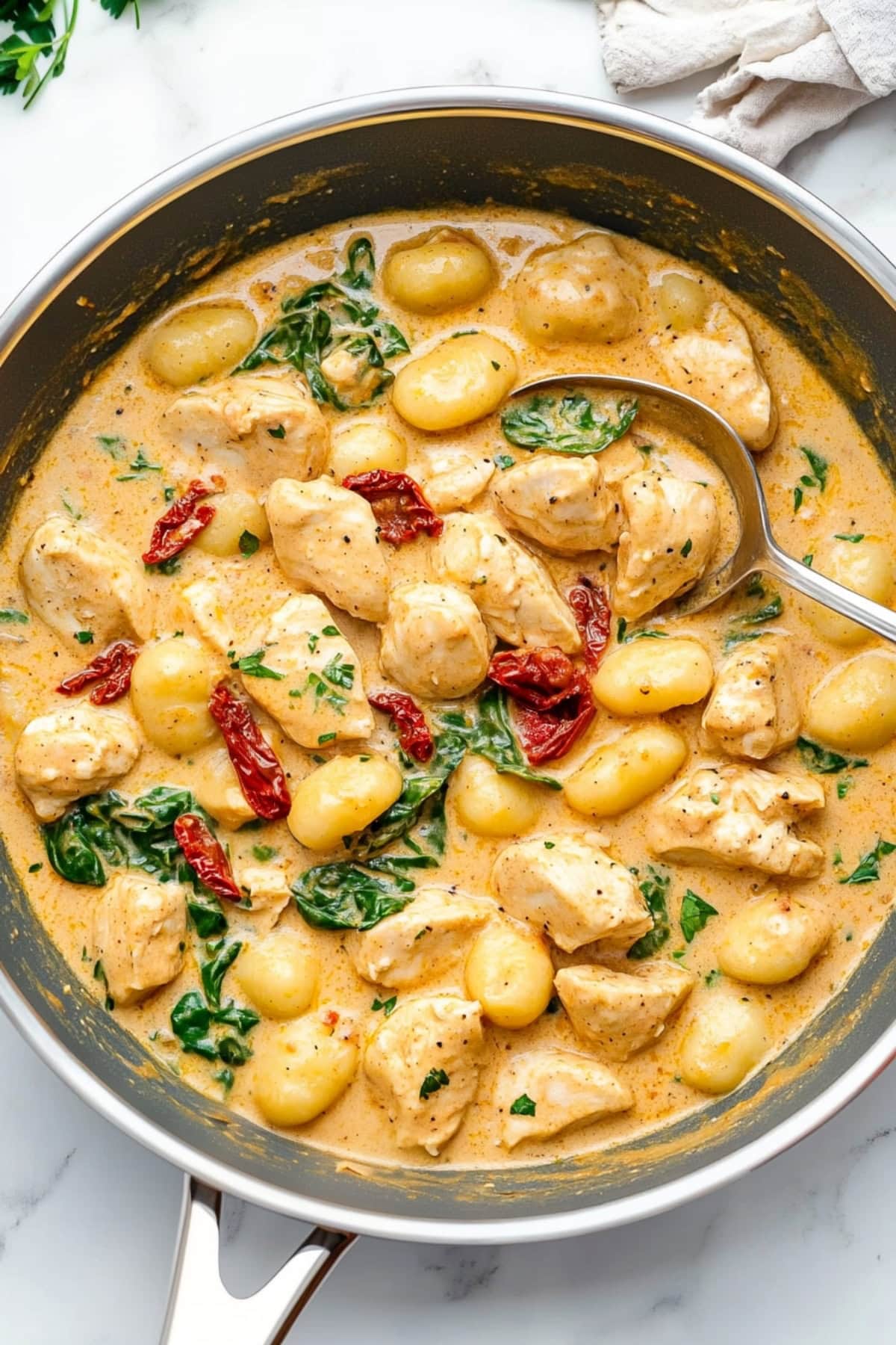 A close-up of creamy chicken and gnocchi served in a white bowl, garnished with fresh herbs.