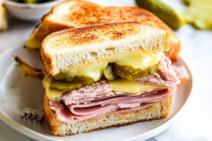 Sliced in half Cuban panini with sliced roast pork, ham, melted cheese and pickles.