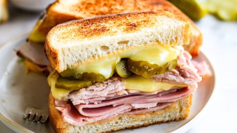 Sliced in half Cuban panini with sliced roast pork, ham, melted cheese and pickles.