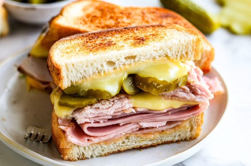 Sliced in half Cuban panini with sliced roast pork, ham, melted cheese and pickles.