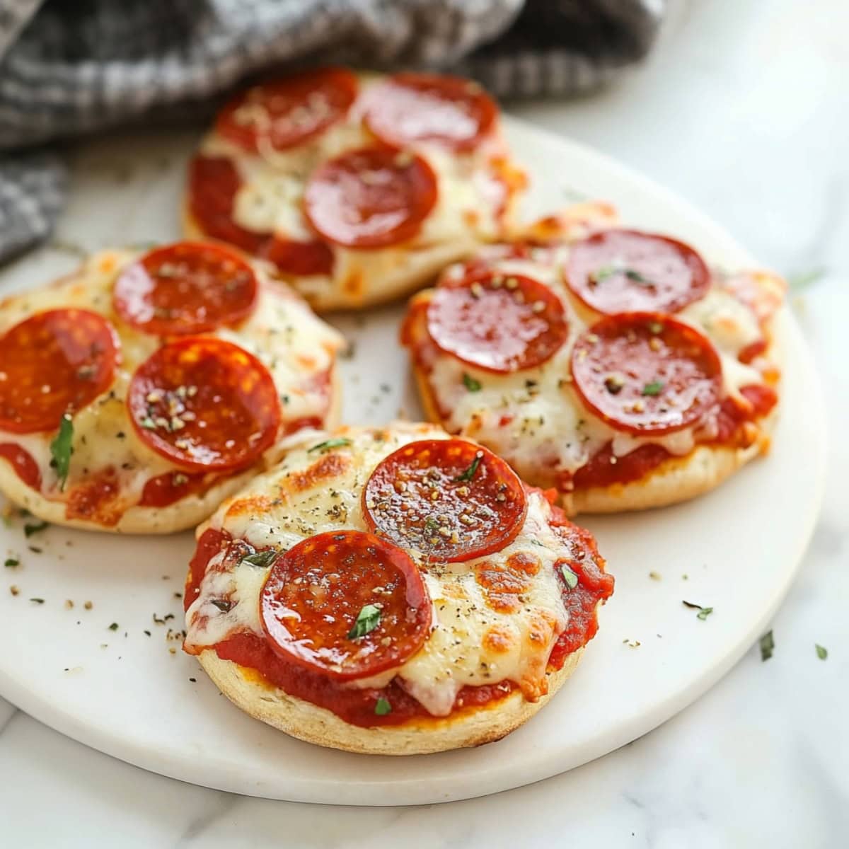 English muffin pizzas with bubbly cheese, golden edges, and a sprinkle of Italian slices and pepperoni.