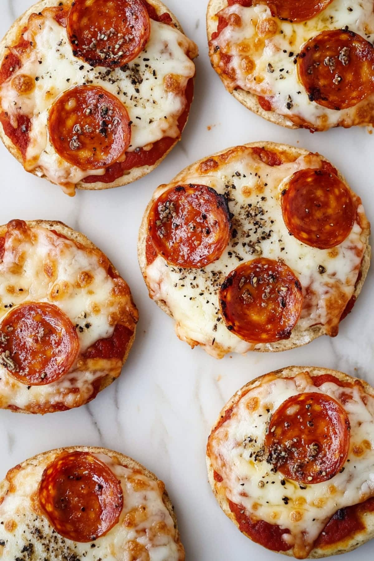 An overhead view of cheesy English muffin pizzas on a white marble table.