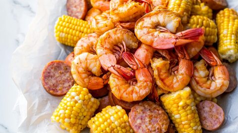 A serving of Frogmore stew with bright red shrimp and golden corn, topped with a sprinkle of chopped parsley and black pepper.