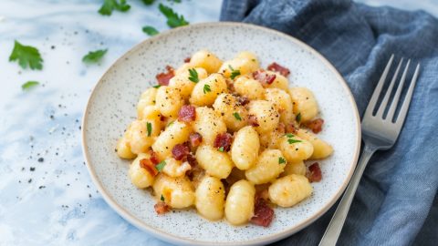 Creamy gnocchi carbonara, with rich cheese and pancetta, served hot on a white ceramic plate.