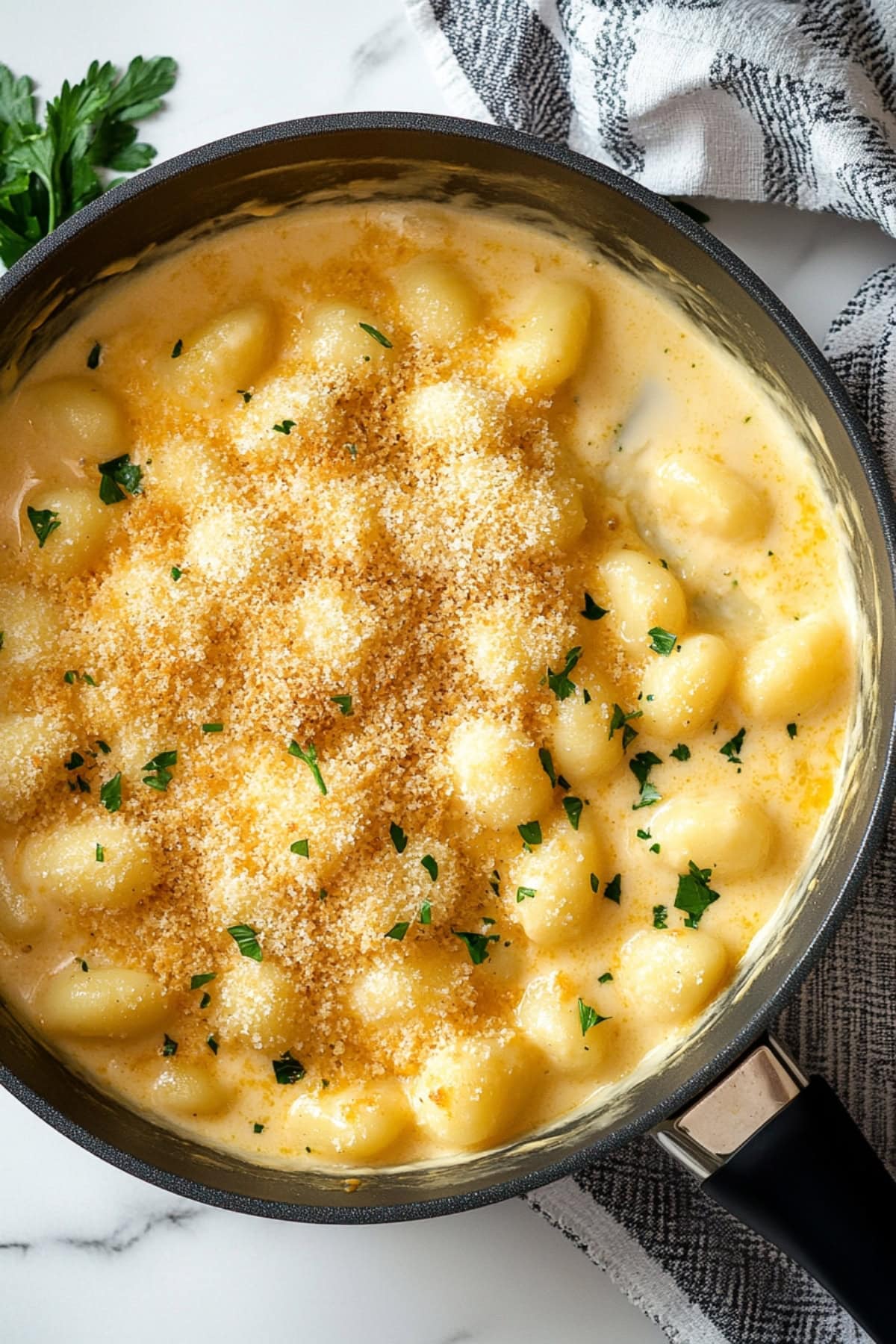 Homemade gnocchi mac and cheese with panko crumbs and parsley, top view in a skillet