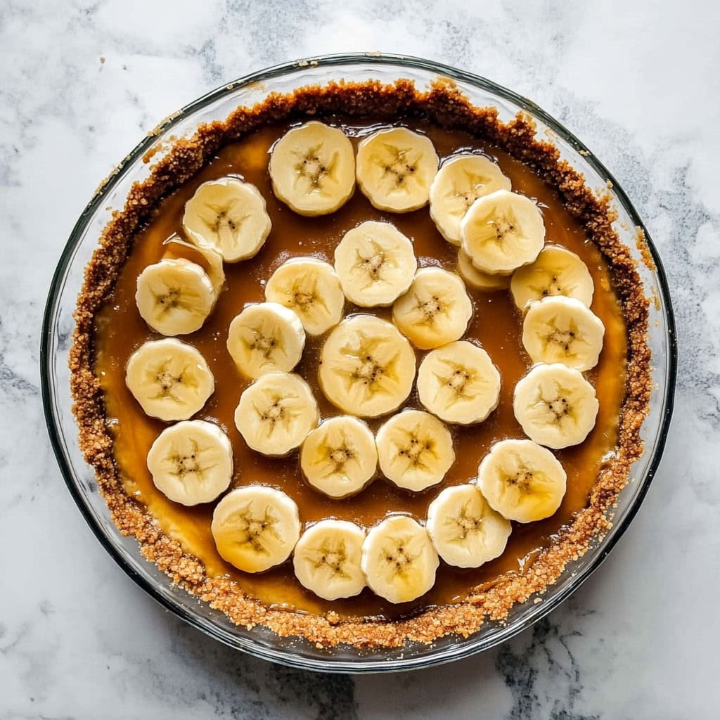 Graham cracker pie crust filled with caramel and topped with fresh banana slices, top view