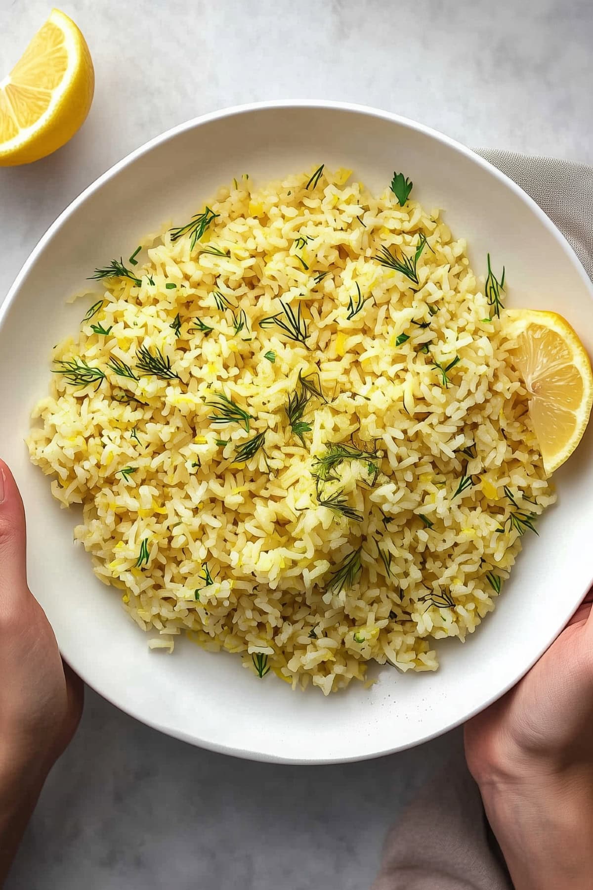 Two hands holding a plate of yellow lemon rice, top view