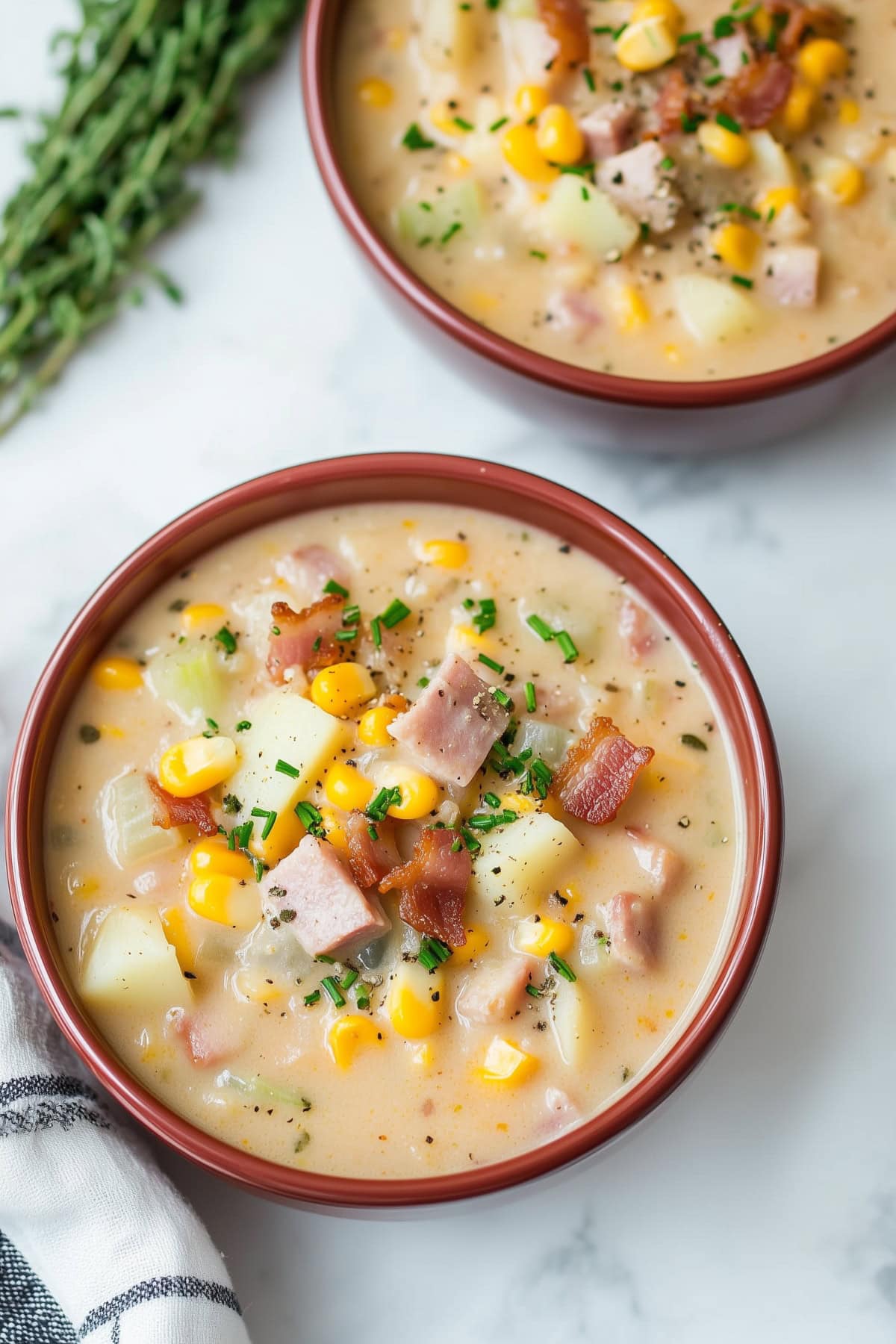 A top-down view of bowls of ham and corn chowder, dotted with fresh herbs.