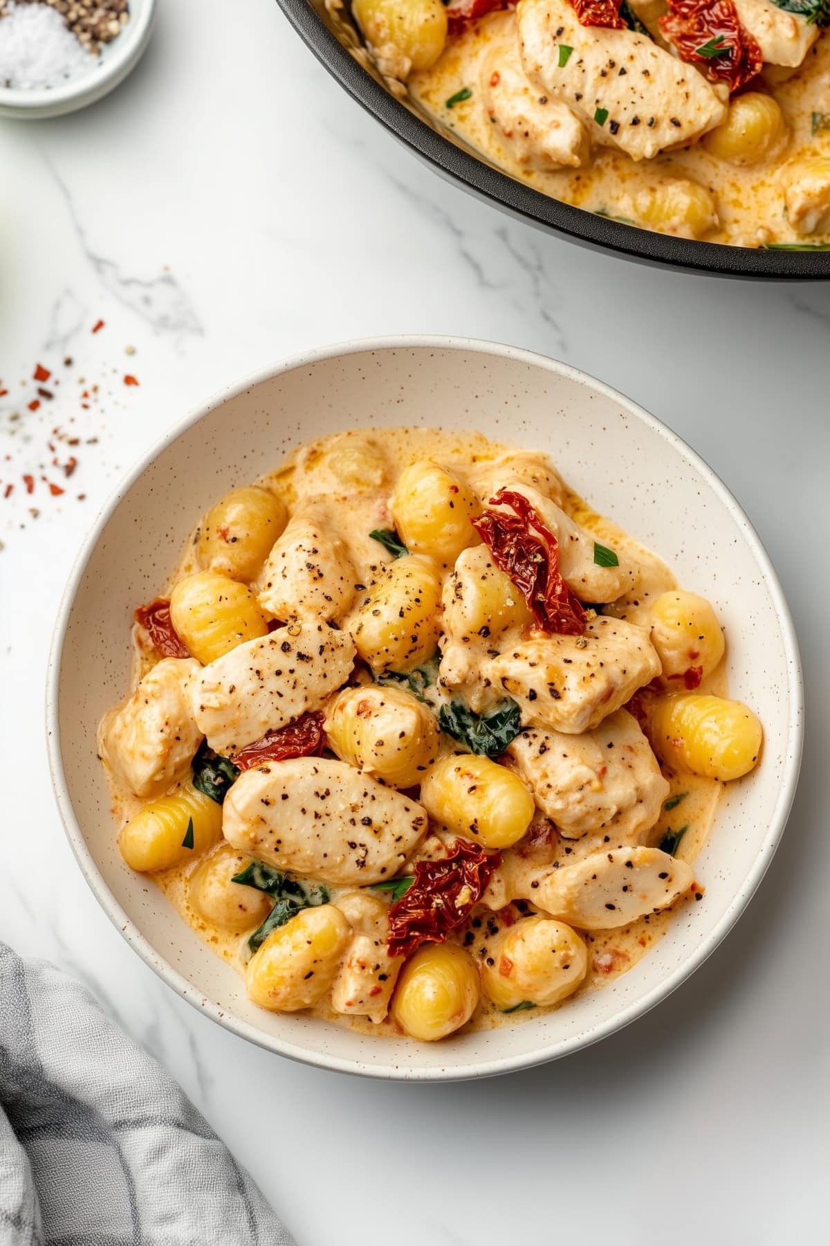 Golden brown chunks of chicken mixed with soft gnocchi in a creamy sauce, served in a bowl and skillet.