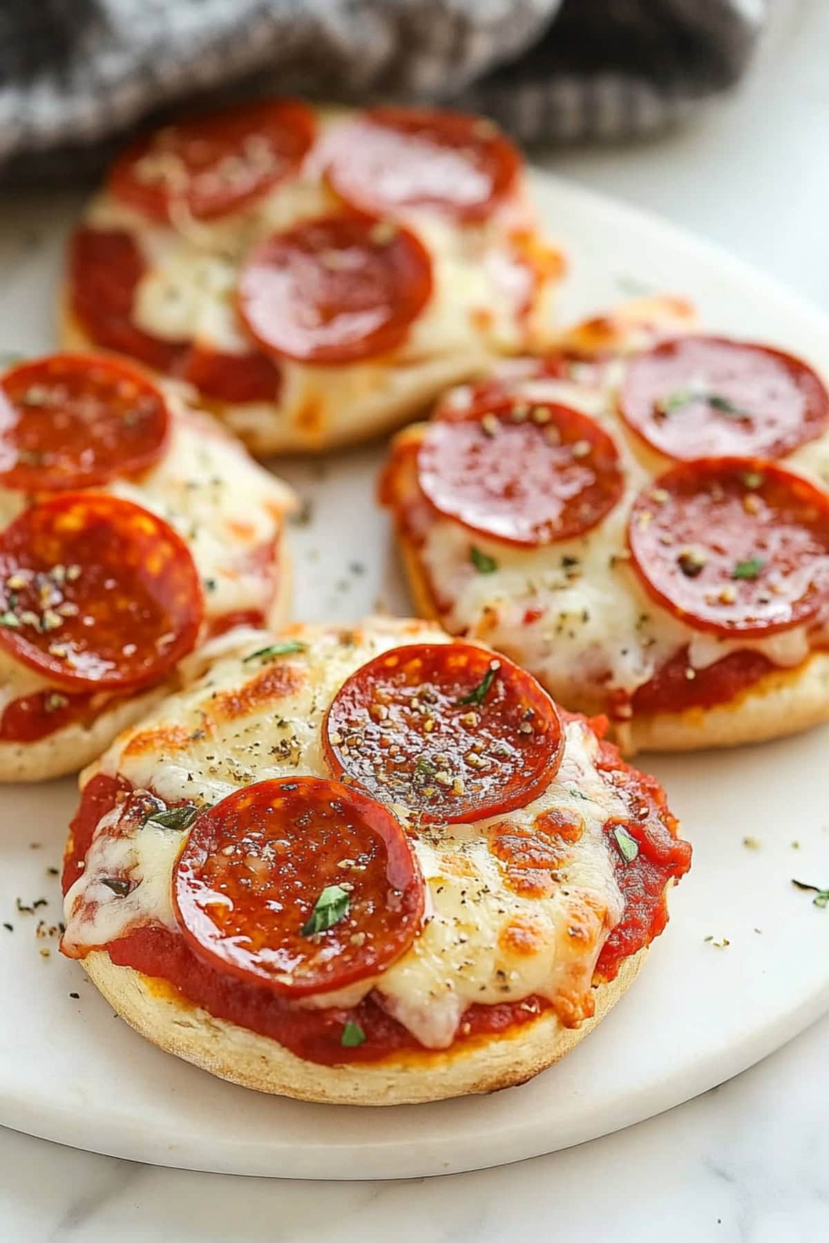 A close-up of a toasted English muffin pizza topped with melted cheese, tomato sauce, and pepperoni slices.