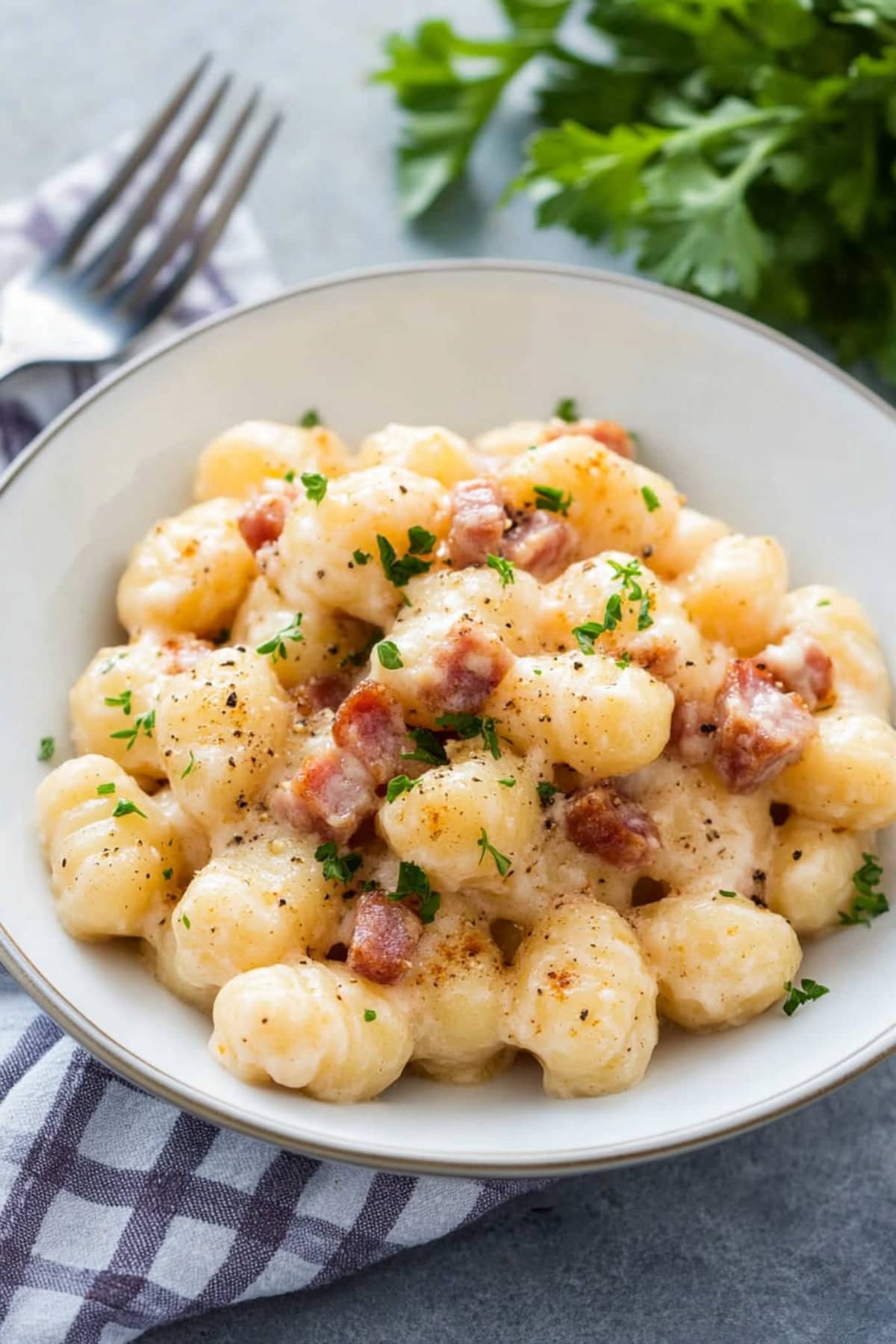 A bowl of gnocchi carbonara with a rich, silky sauce and garnished with freshly ground black pepper and parsley.