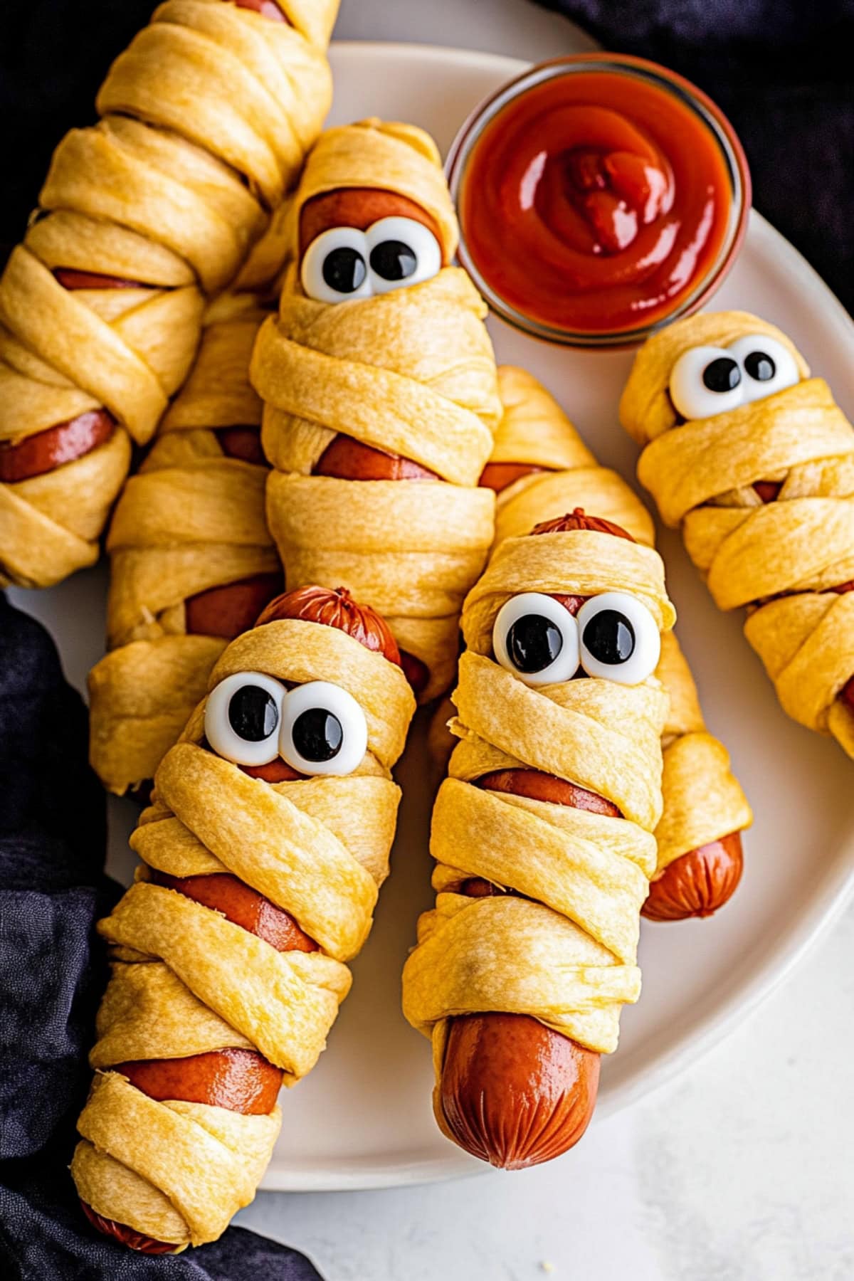 Mummy hot dogs with flaky dough and eye candies, served with ketchup for dipping