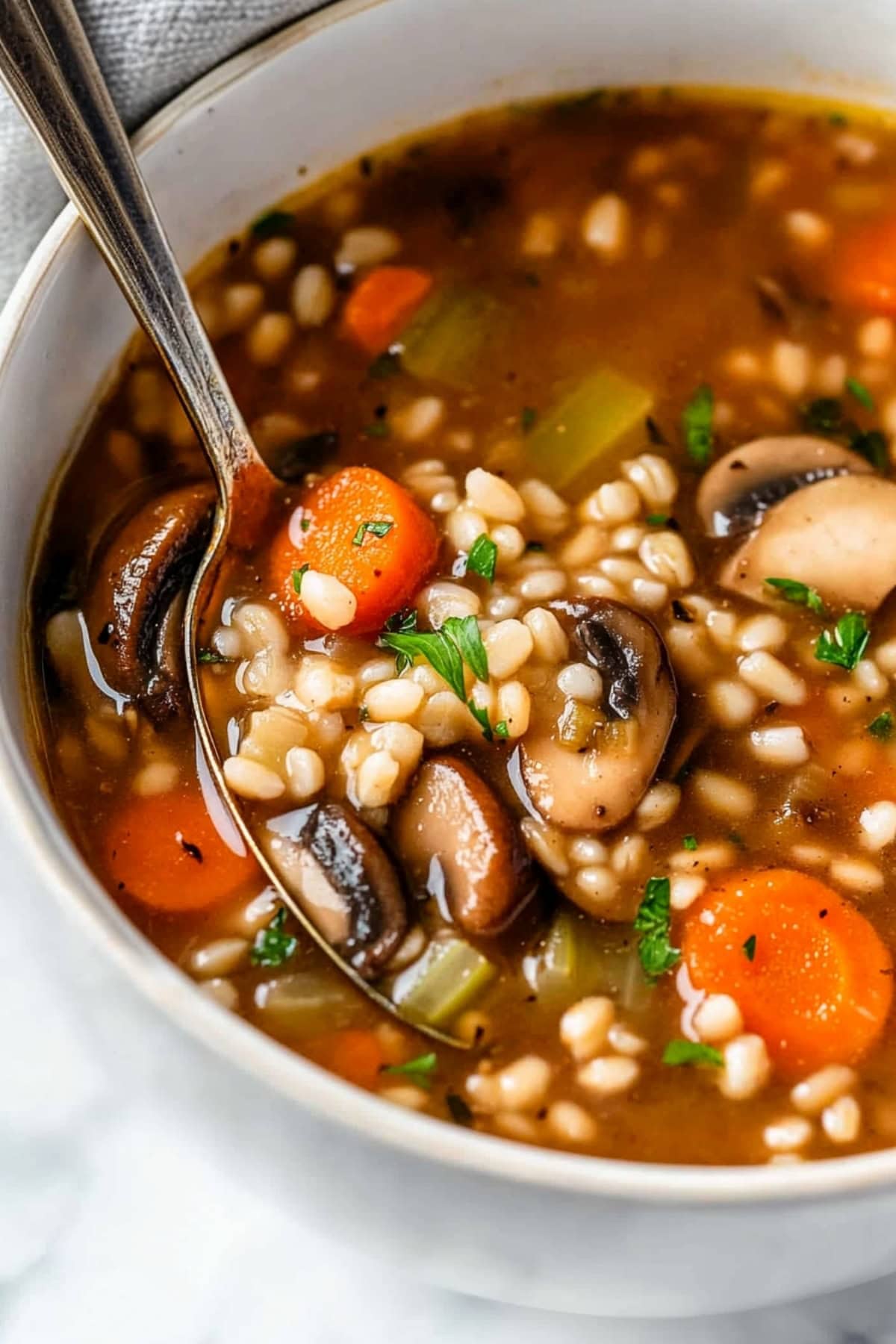 Steaming mushroom barley soup, garnished with fresh parsley and served in a white bowl.