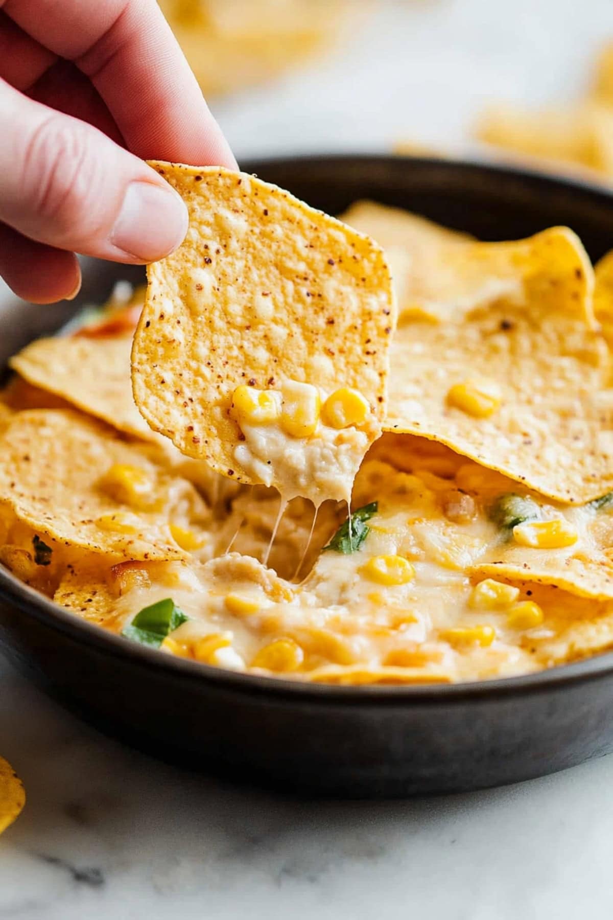 A hand dipping a tortilla chip into a skillet of hot corn dip.