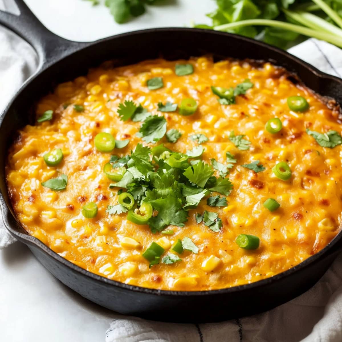 Bubbling hot corn dip served in a skillet, topped with melted cheese, jalapeños, and garnished with cilantro.