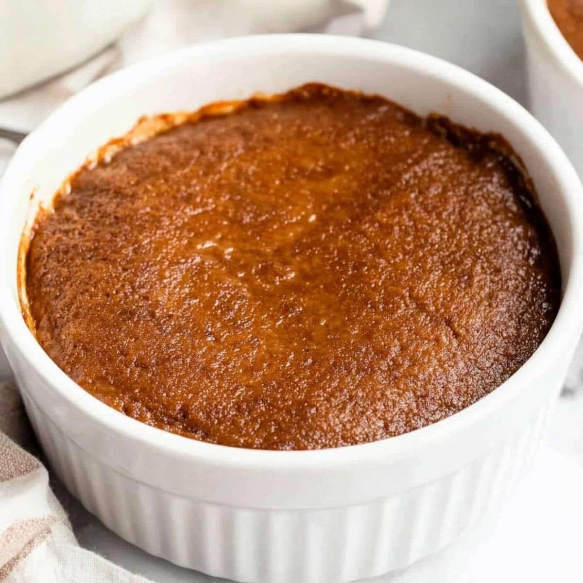 Close-up of a baked Indian pudding, showing the creamy cornmeal base with hints of molasses and granulated sugar.