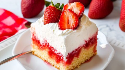 Square slice serving of jello poke cake garnished with fresh slices of strawberries.