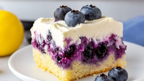 A slice serving of lemon blueberry poke cake garnished with fresh berries served in a white plate.