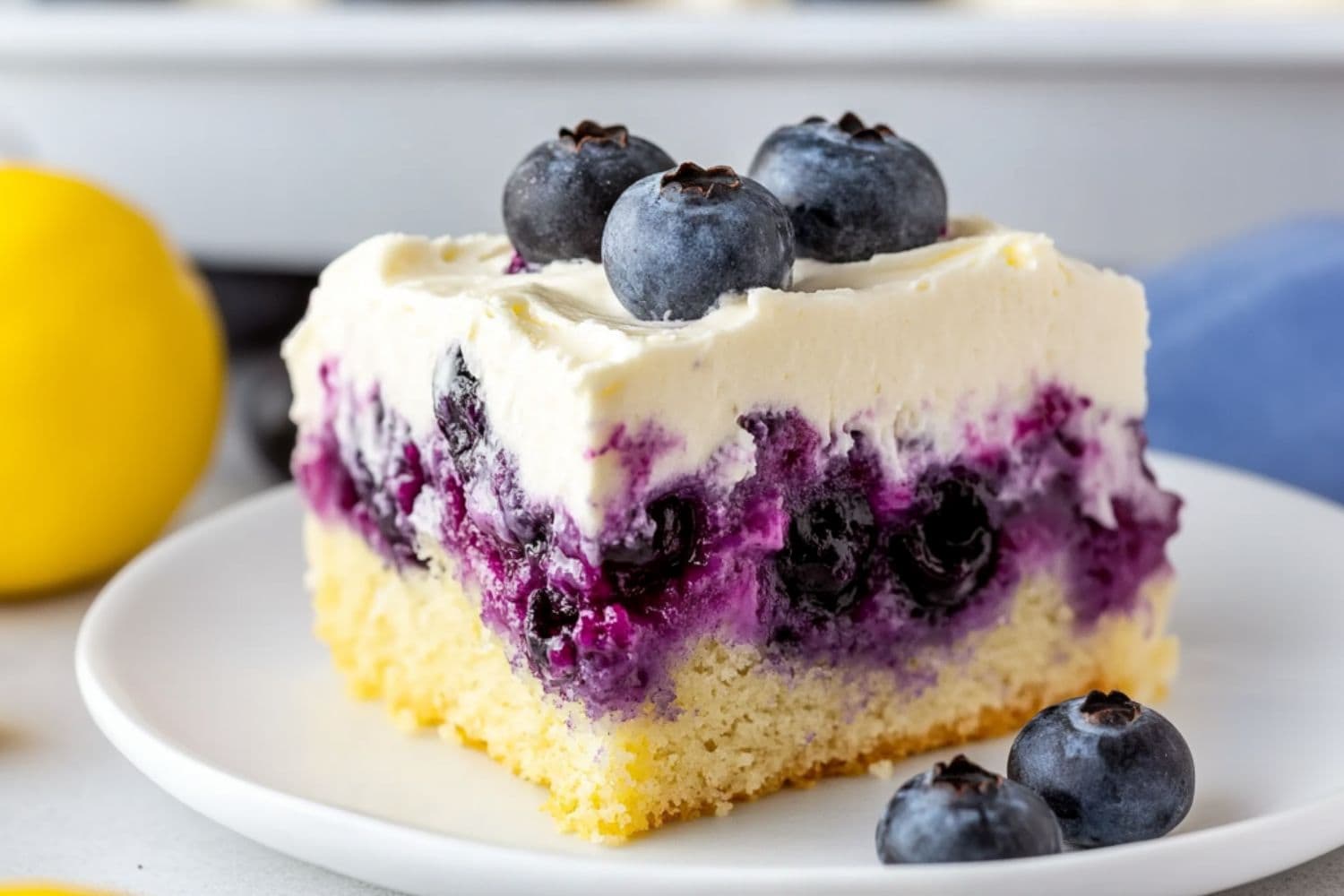 A slice serving of lemon blueberry poke cake garnished with fresh berries served in a white plate.