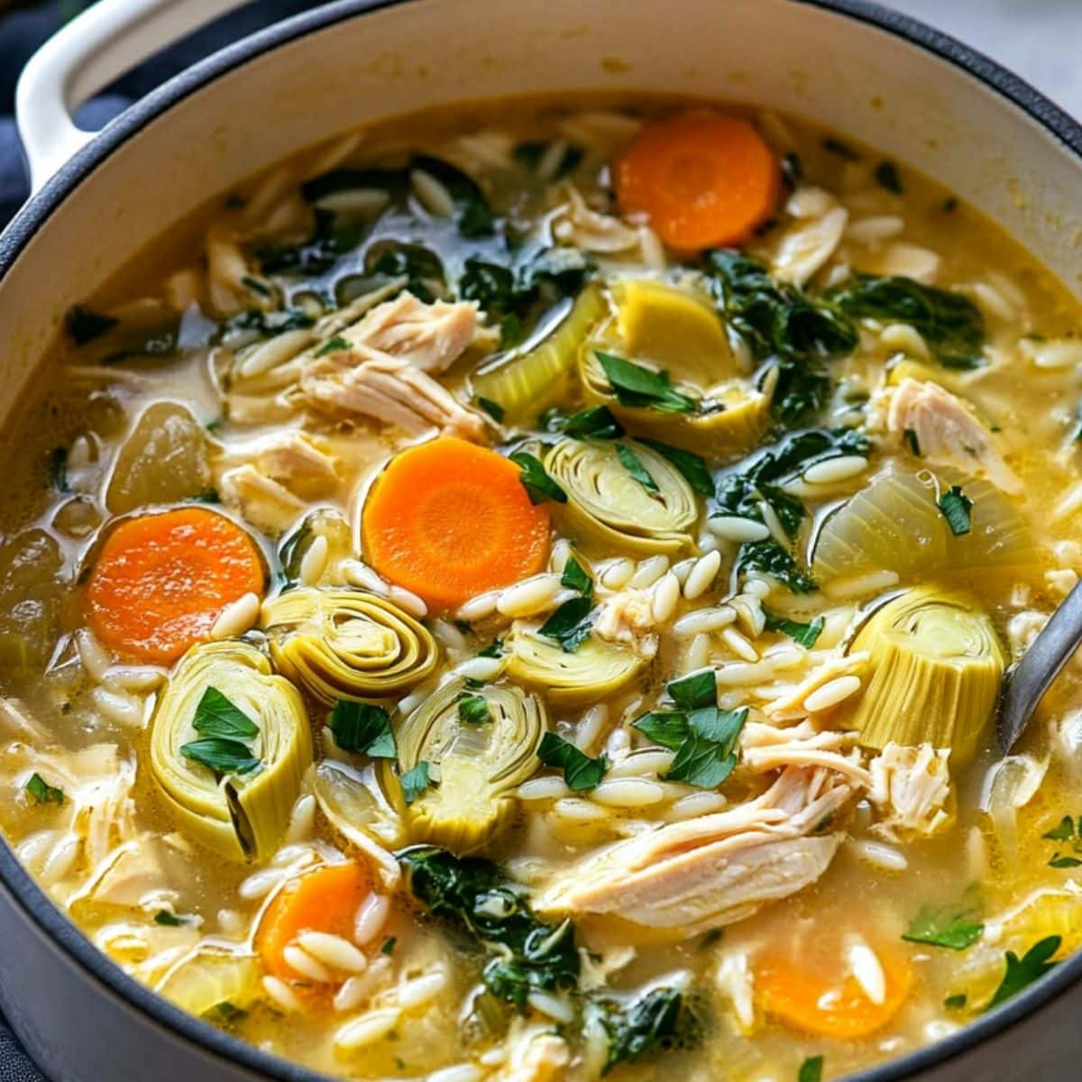 Lemon artichoke chicken soup in a white pot.