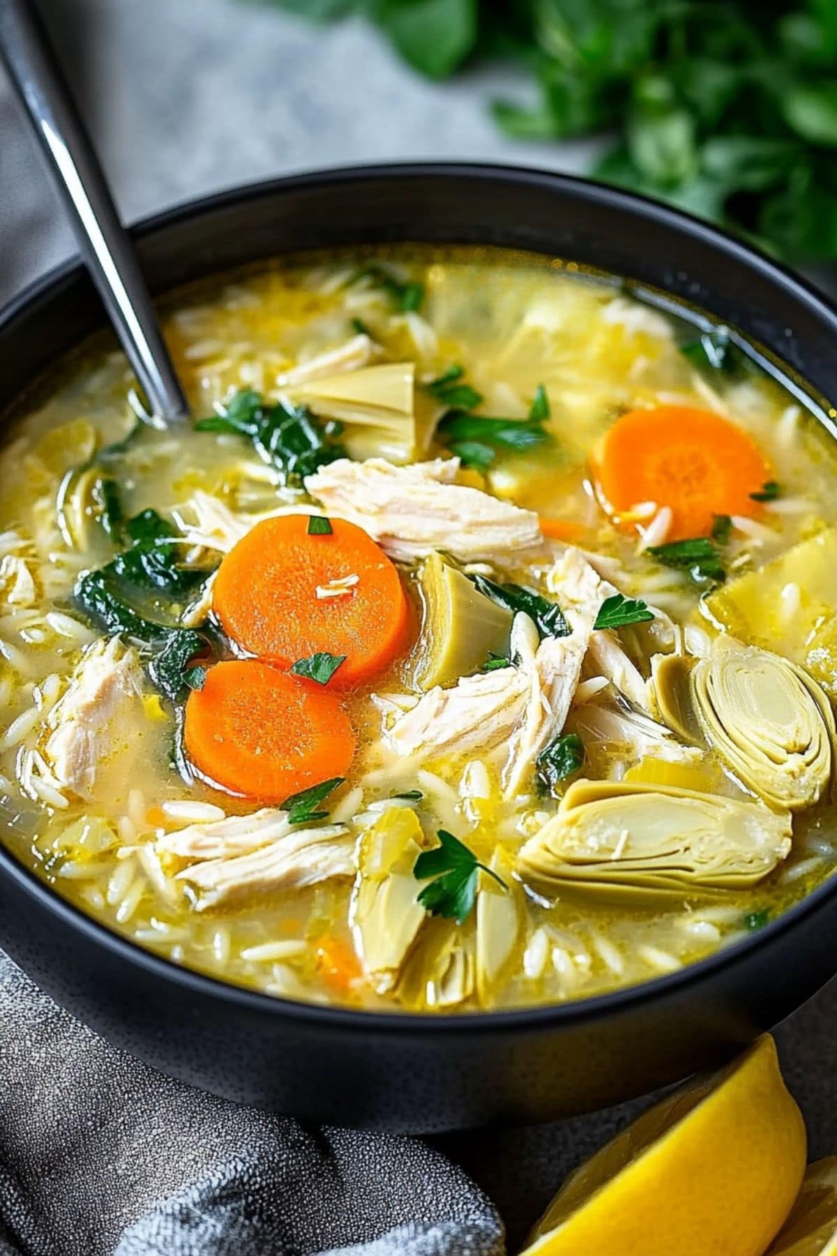 Lemon chicken artichoke soup with carrots, shredded chicken, spinach and orzo pasta served in a bowl.