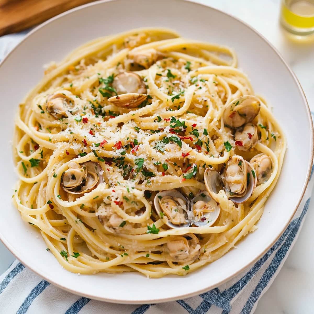 Linguine with clam sauce served in a white plate, spinkled with parmesan cheese.
