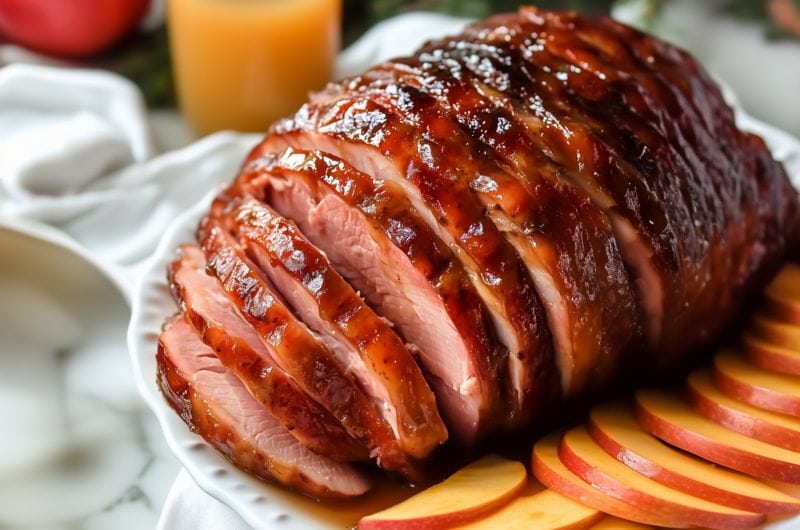 A perfectly roasted ham with a sweet maple glaze served in a white plate.